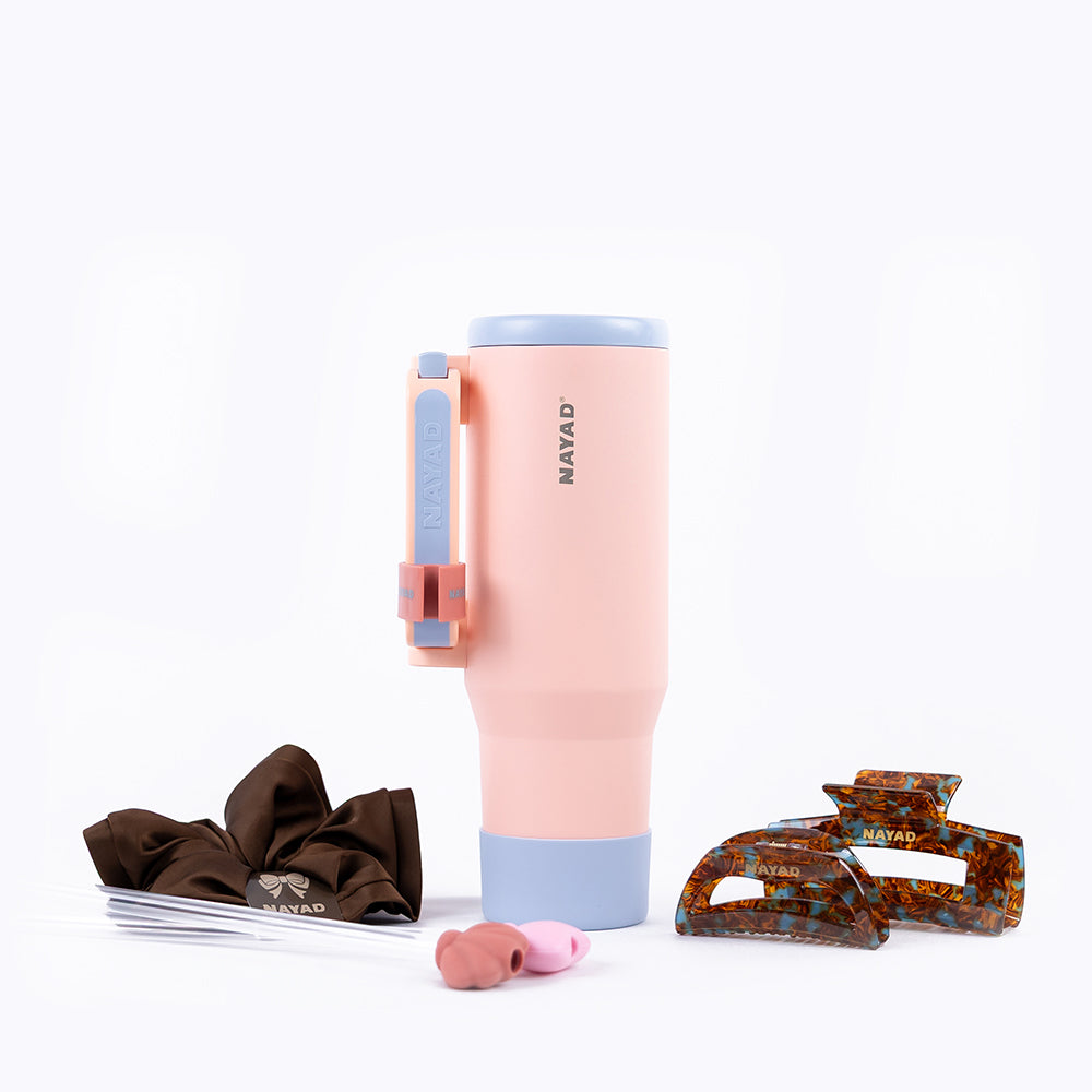 Pink tumbler with blue accents, brown hair tie, pink earbuds, and tortoiseshell hair clips on a white background.