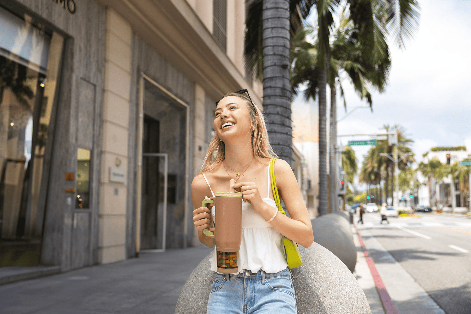 Woman walking on a city street holding a nayad cup and smiling.