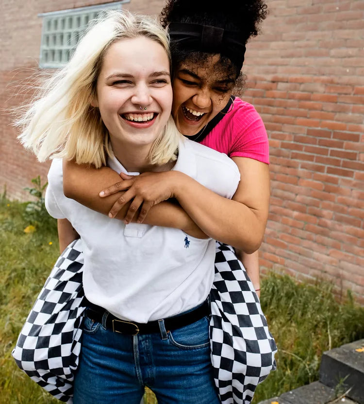 Two friends hugging outdoors with a brick building in the background