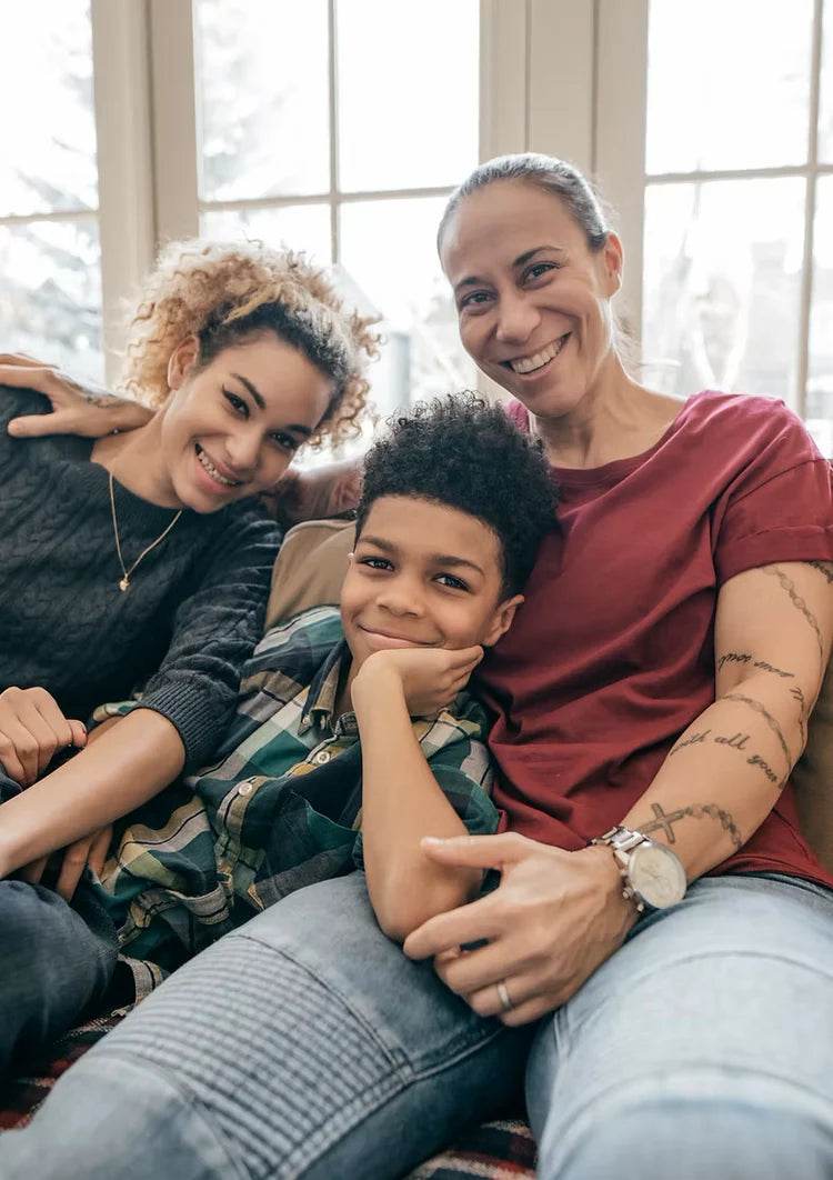 Two women and a child sitting together indoors, smiling.