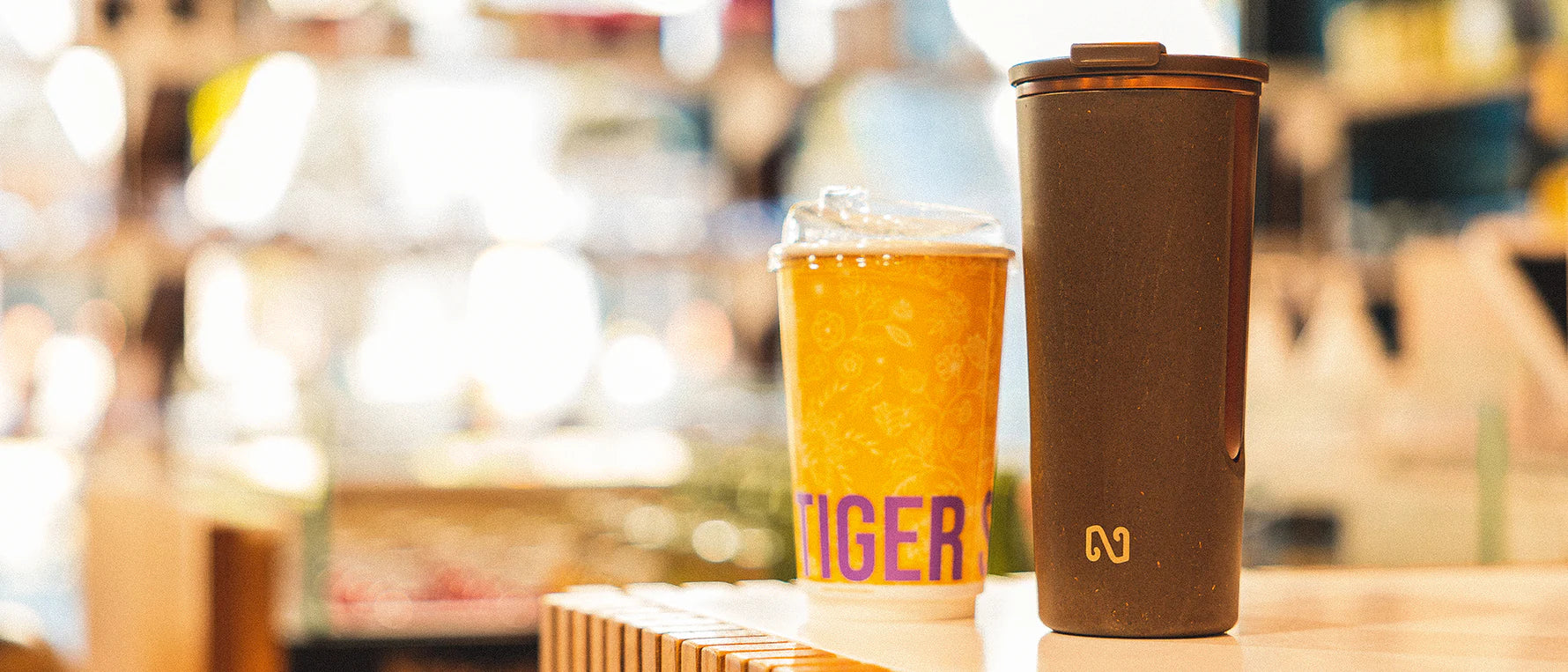 Two drinks, one in a glass with a Tiger logo and the other in a brown tumbler, on a blurred background.