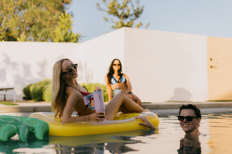 Two women on a pineapple-shaped inflatable raft in a pool with a man in the water.