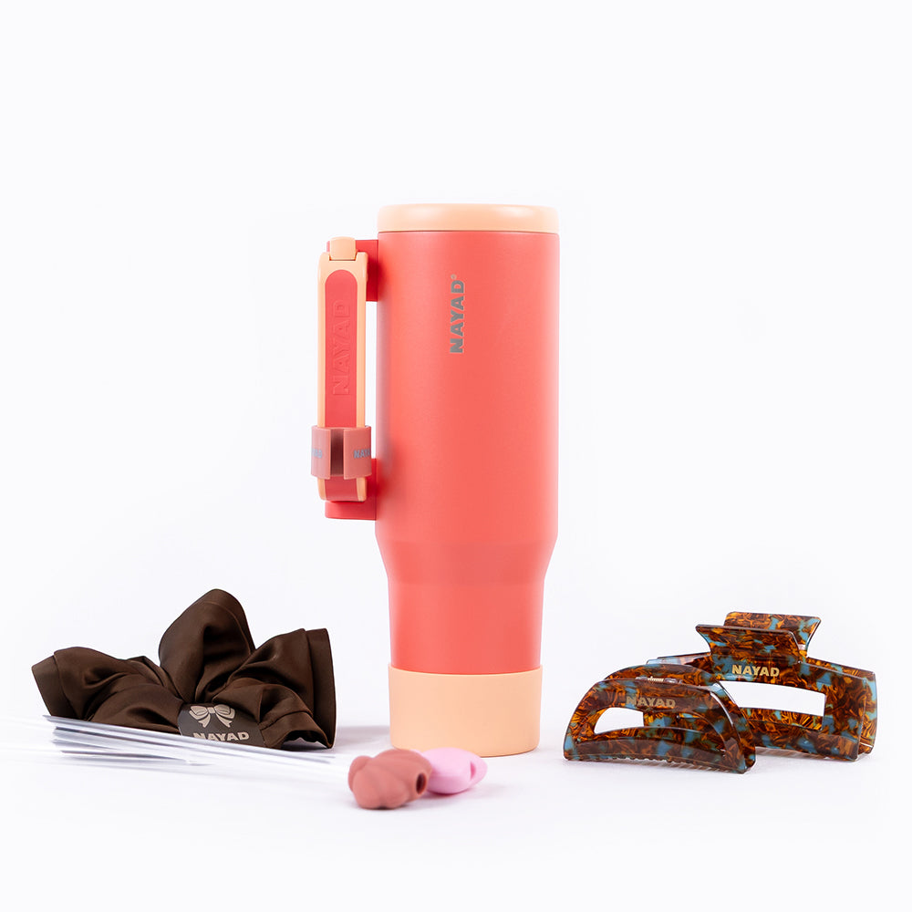 Coral tumbler with beige lid, brown hair clips, and pink earbud on a white background