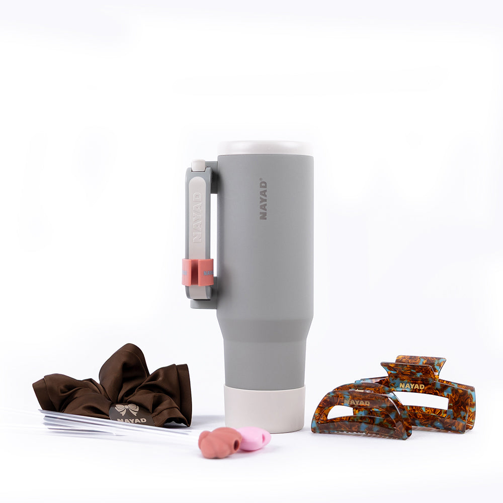 Gray tumbler with handle, brown hair clips, pink hair clip, and comb on a white background