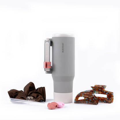 Gray tumbler with handle, brown hair clips, pink hair clip, and comb on a white background