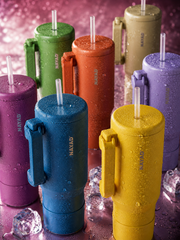 Colorful insulated tumblers with handles on a reflective surface