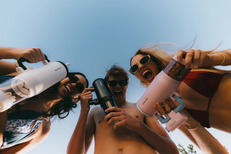 Three people holding white, pink and black water bottles against a clear blue sky.
