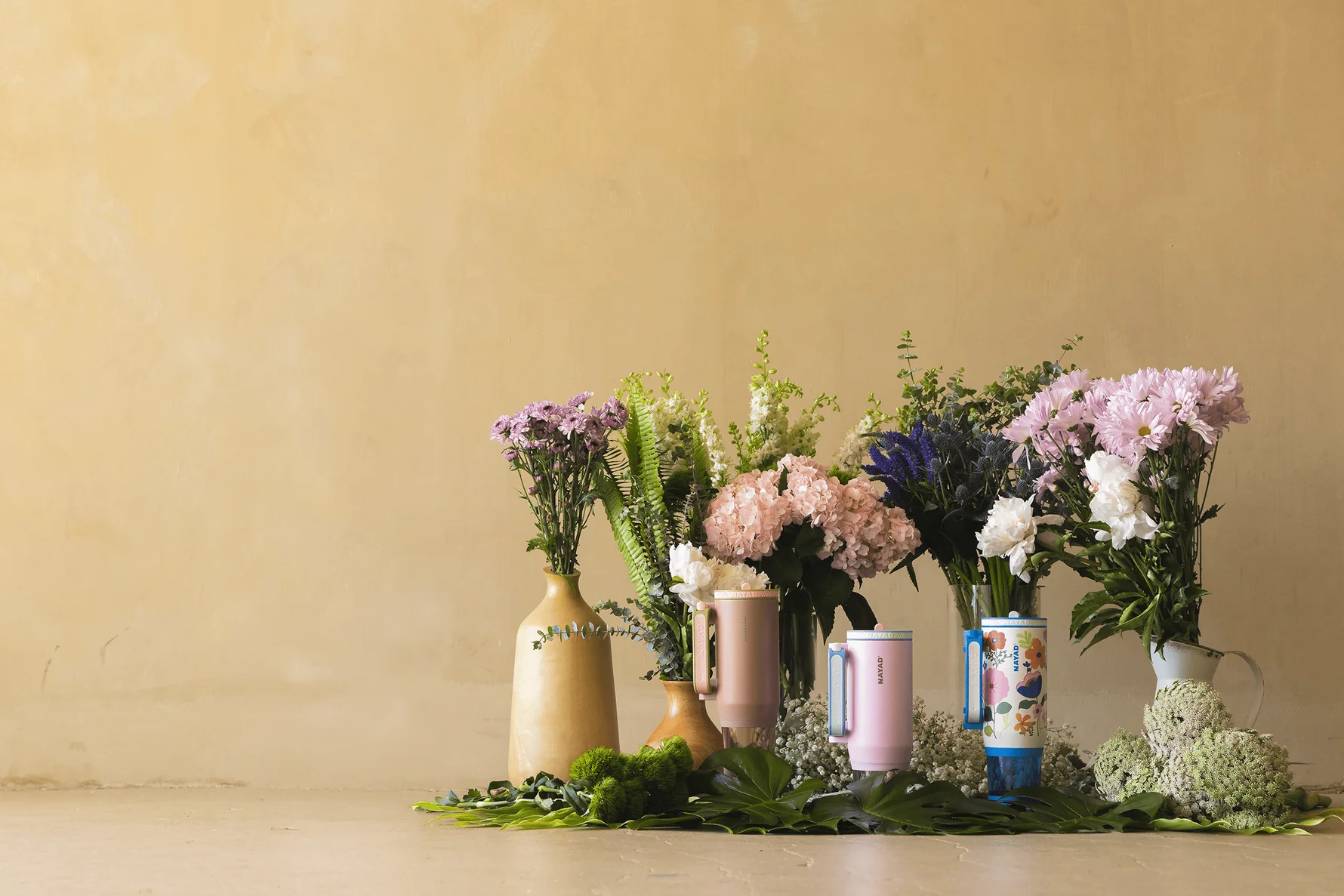 Five vases with flowers  behind nayad water tumblers on a beige background