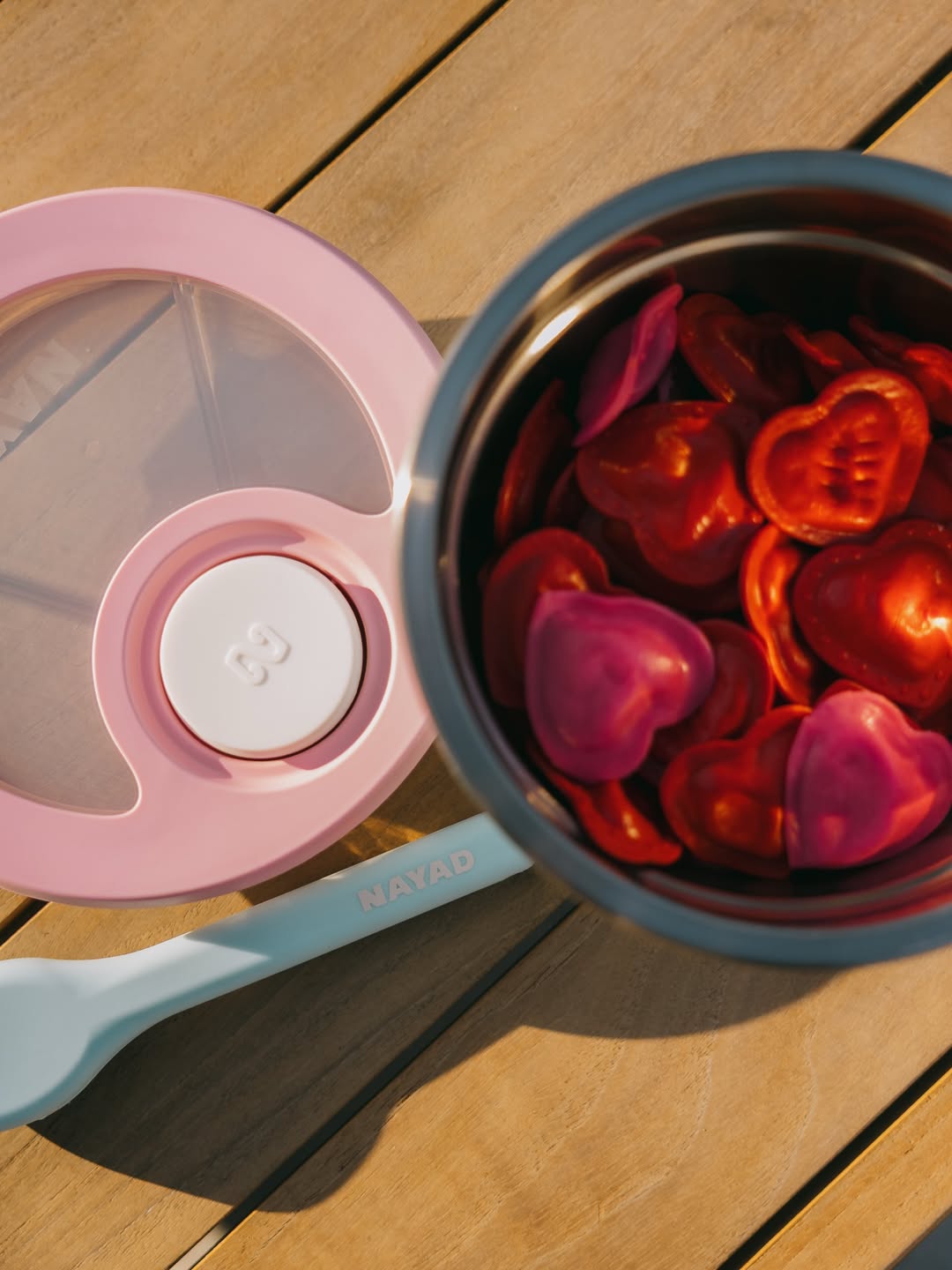Pink snack container with heart-shaped silicone pieces on a wooden surface